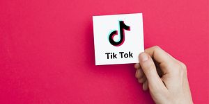 En hand håller i ett vitt kort med TikTok logga på, mörkrosa bakgrund. 