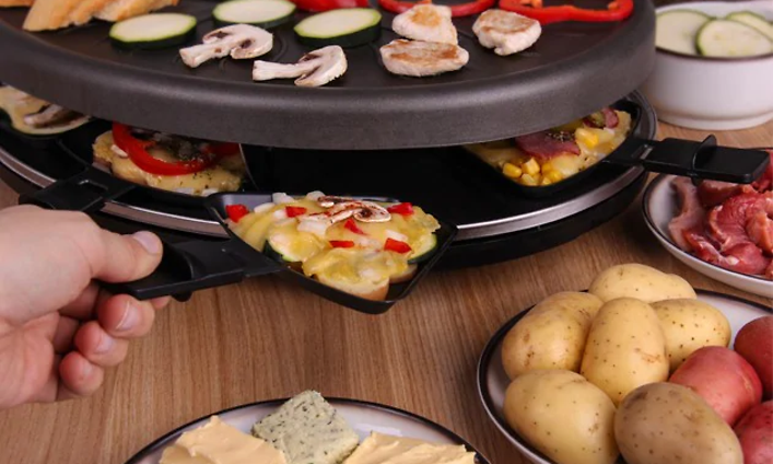 Person placing raclette pan in round raclette with food