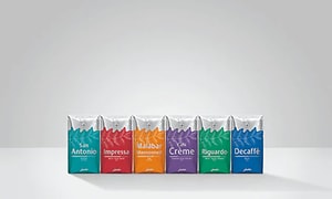 En rad med förpackningar i olika färg som innehåller kaffebönor. San Antonio, Impressa, Malabar, Caffe Creme osv