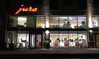En stor upplyst kontorslokal på två våningsplan med Juras logga i orange färg på utsidan ovan entren.