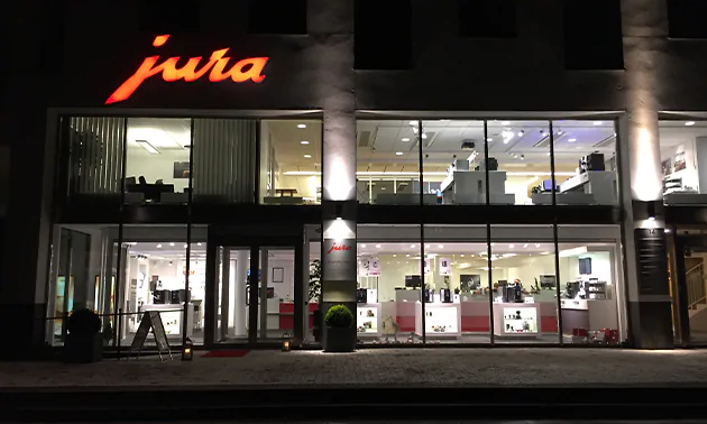En stor upplyst kontorslokal på två våningsplan med Juras logga i orange färg på utsidan ovan entren.  
