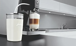 Kaffemaskin från Jura med en milkskummare vid sidan och en färdigbryggd kaffe latte. 