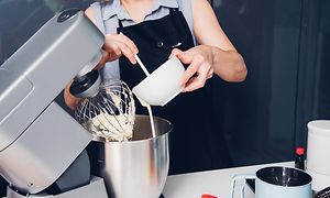Kvinna som bakar en kaka med en köksmaskin