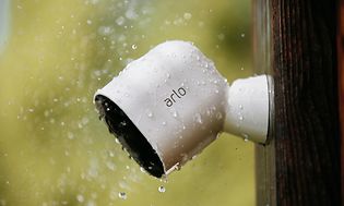 Vit övervakningskamera från Arlo på husvägg i regnet. 