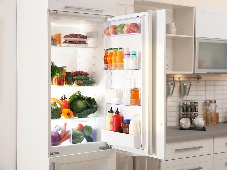 Integrerat kylskåp med öppen dörr i ett vitt kök. 