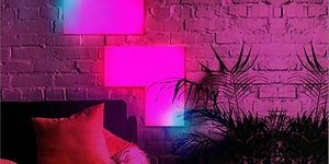 LIFX Tile med rosa och blått ljus på vägg i vardagsrum. Hörnet på en soffa och en stor krukväxt syns också. 