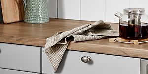 Bänkskiva i laminat med trädesign och en tekanna ovanpå och en kökshandduk. 