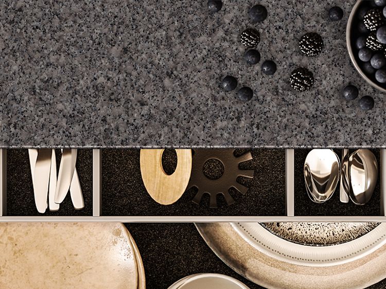 Detaljbild på bänkskiva i granit med öppen kökslåda med bestick i. 