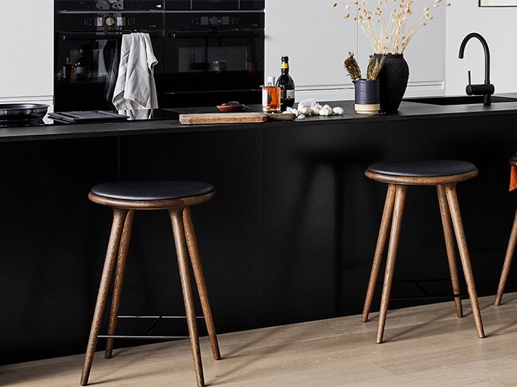 Köksö med svart bänkskiva i dekton material med barstolar och köksprylar på bänken.