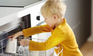 Ung pojke i gul tröja som sätter in muggar i diskmaskinen