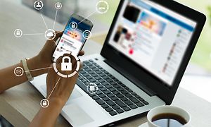 Kvinna som håller en mobiltelefon där en illustrerad ikon med ett hänglås syns bredvid en bärbar dator