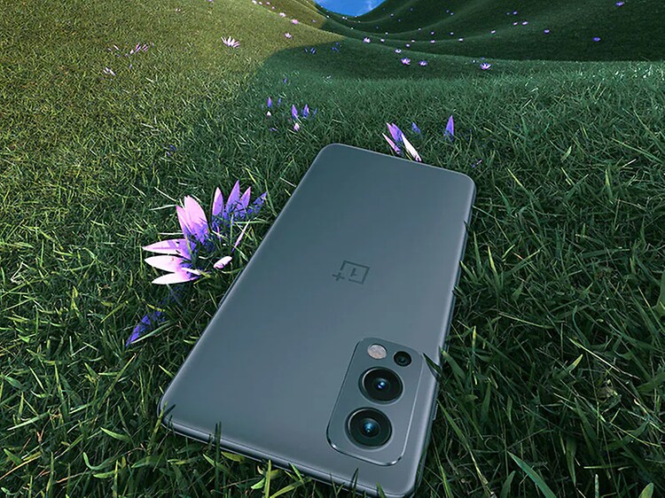 OnePlus Nord 2 som ligger på en gräsmatta med en lila blomma som sticker fram bredvid. 