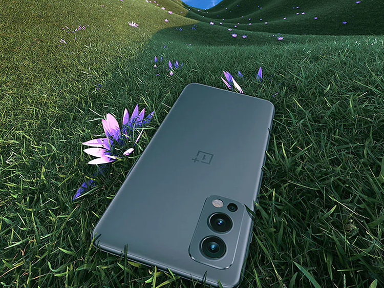 OnePlus Nord 2 som ligger på en gräsmatta med en lila blomma som sticker fram bredvid.