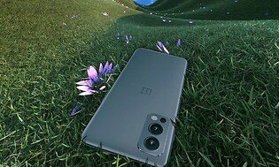 OnePlus Nord 2 som ligger på en gräsmatta med en lila blomma som sticker fram bredvid. 