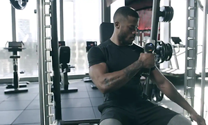 Man som sitter i en träningsmaskin på ett gym och använder en Hypervolt-massagepistol.