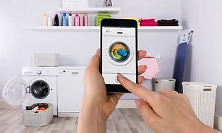 Tvättmaskin med wifi: Hand som håller upp en mobil med tvättmaskinsapp.