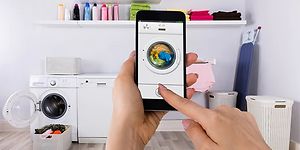 Hand som håller upp en mobil med tvättmaskinsapp på skärmen i en tvättstuga.