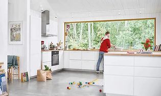 En man som diskar i ett vitt kök med en massa leksaker på golvet.