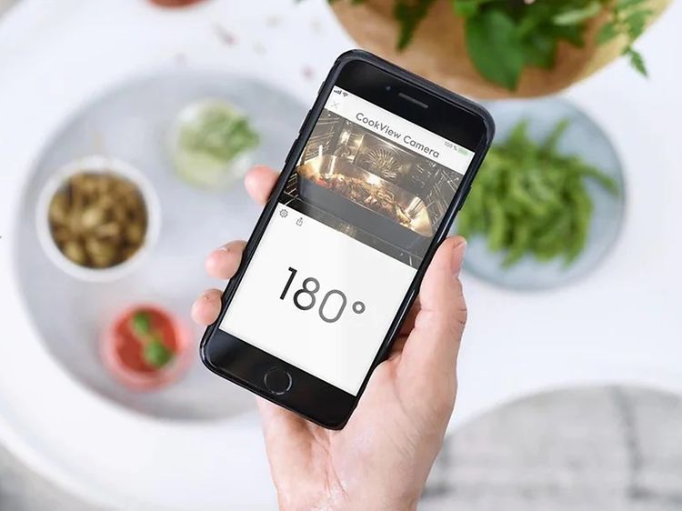 En hand som håller upp en mobil med en app som visar en kameravy från en smart ugn och ugnstemperatur.