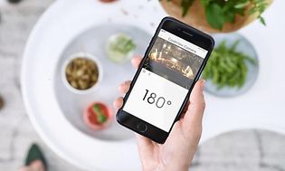 En hand som håller upp en mobil med en app som visar en kameravy från en smart ugn och ugnstemperatur.