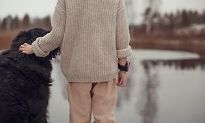 Bild bakifrån på ett barn med en Xplora X5-smartklocka på handleden som står bredvid en hund och ser bort, ut över en sjö.