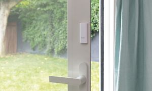 Smart sensor, en vit liten dosa, placerad på altandörr med glas och vit dörrkarm.
