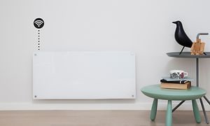 Ett vitt element på en ljus vägg och en liten pall och ett bord vid sidan av. 