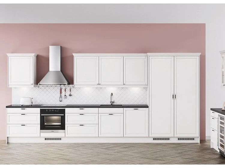 Vitt kök med silverfärgad vägghängd köksfläkt och rosa tapeter.