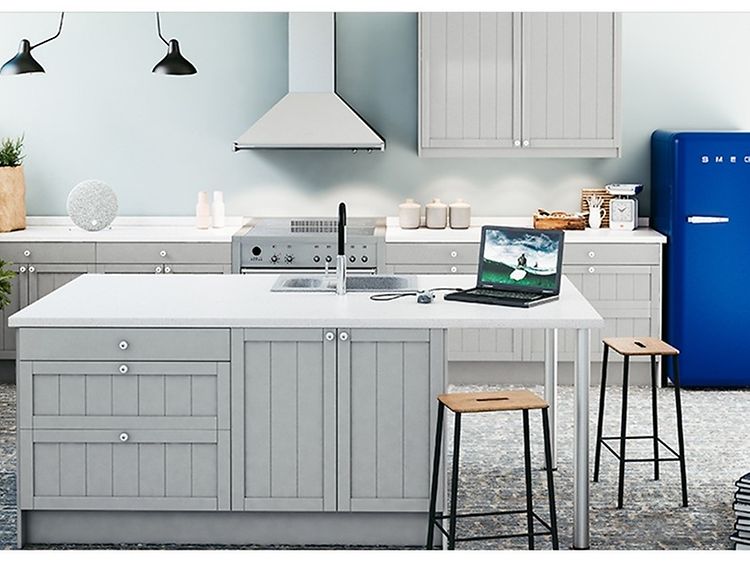 Ljust kök med en vit väggmonterad köksfläkt och ett blått kylskåp från Smeg och köksö med stolar.