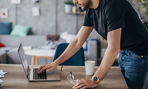 Man leaning over table while working on his Lenovo ThinkPad laptop