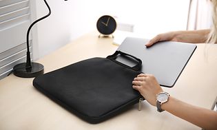 Kvinna stoppar ner en bärbar dator i ett svart fodral på ett bord. 