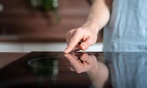 Person som trycker ett finger mot knapparna på en induktionshäll.
