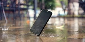 Mobiltelefon som ramlar ner på gatan och träffar asfalten så att skärmen krossas. Regndroppar faller och skvätter vatten. 