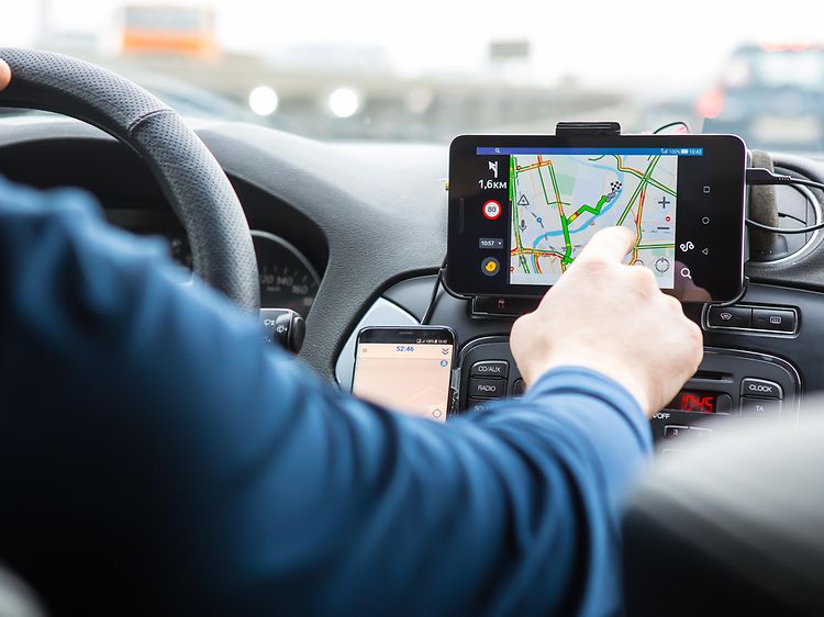 Man som använder en GPS i en bil, pekar med handen på skärmen som sitter vid sidan a ratten. 