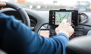 Man som använder en GPS i en bil, pekar med handen på skärmen som sitter vid sidan a ratten. 