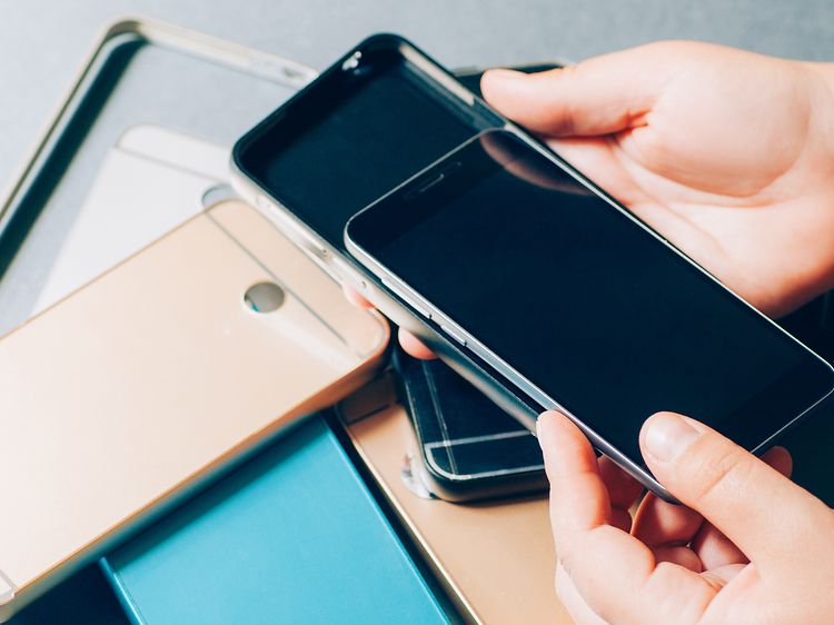 Mobiltelefon och flera olika skal i en hög på ett bord. En hand som sätter mobilen i ett av skalen.
