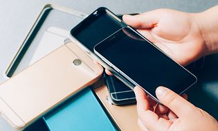 Mobiltelefon och flera olika skal i en hög på ett bord. En hand som sätter mobilen i ett av skalen.