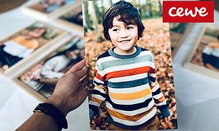 En hand som håller upp ett stor fotografi på en pojke randig tröja, i bakgrunden syns fler fotoutskrifter.