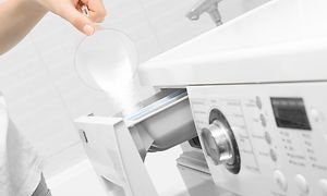 Person som häller en skopa pulvertvättmedel i facket för tvättmedel på en tvättmaskin.