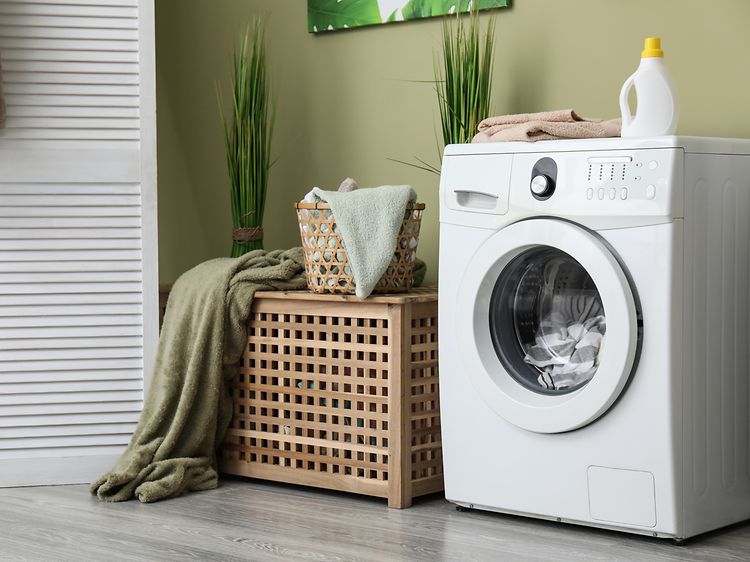 Tvättmaskin i modern tvättstuga placerad mot en grön vägg med träfärgad bänk med förvaring bredvid och en vit garderob. 