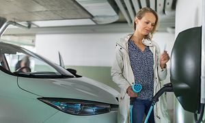 Kvinna som håller en elbilsladdare i ett garage