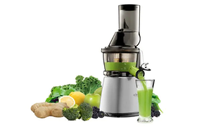 Slowjuicer med grön juice på väg ut i ett glas, vid sidan står en massa gröna frukter och grönsaker.