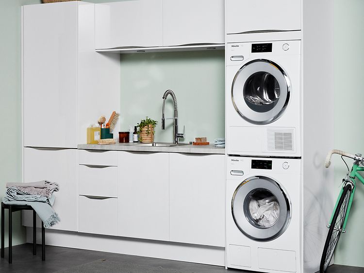 Tvättmaskin och torktumlare i tvättstuga med vit och grön interiör.