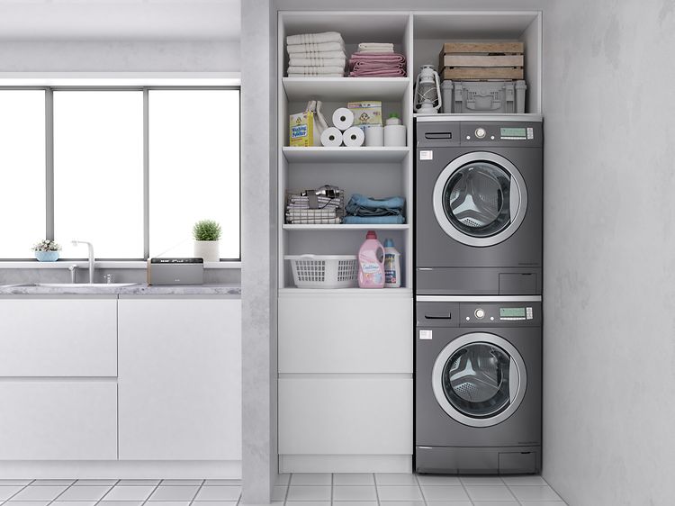 Stapel med tvättmaskin och torktumlare ovanpå varandra i  tvättstuga med vit och grå interiör. 