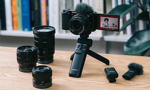 Kamera på en liten tripod med olika objektiv och tillbehör bredvid den