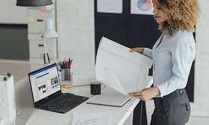 Kvinnlig arkitekt ser på sketch med Lenovo ThinkPad på bordet bredvid