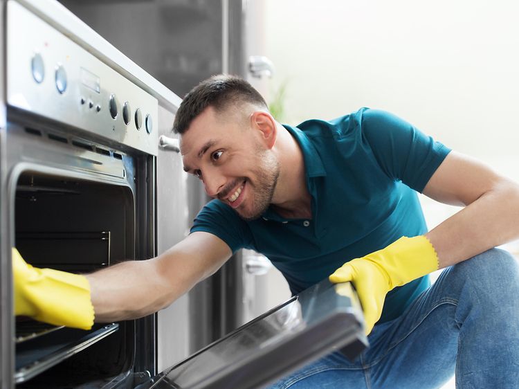 MDA-Dishwasher-Man med gula gummihandskar gör rent i en ugn