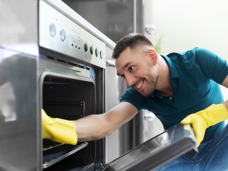 MDA-Dishwasher-Man med gula gummihandskar gör rent i en ugn