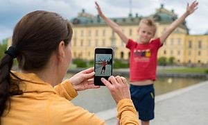 En kvinna håller upp en mobiltelefon och tar en bild av en pojke framför ett slott. 