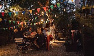 Kvinna tar en bild av flera personer som samlats på en trädgårdsfest bland träden med ljusslingor och vimplar.